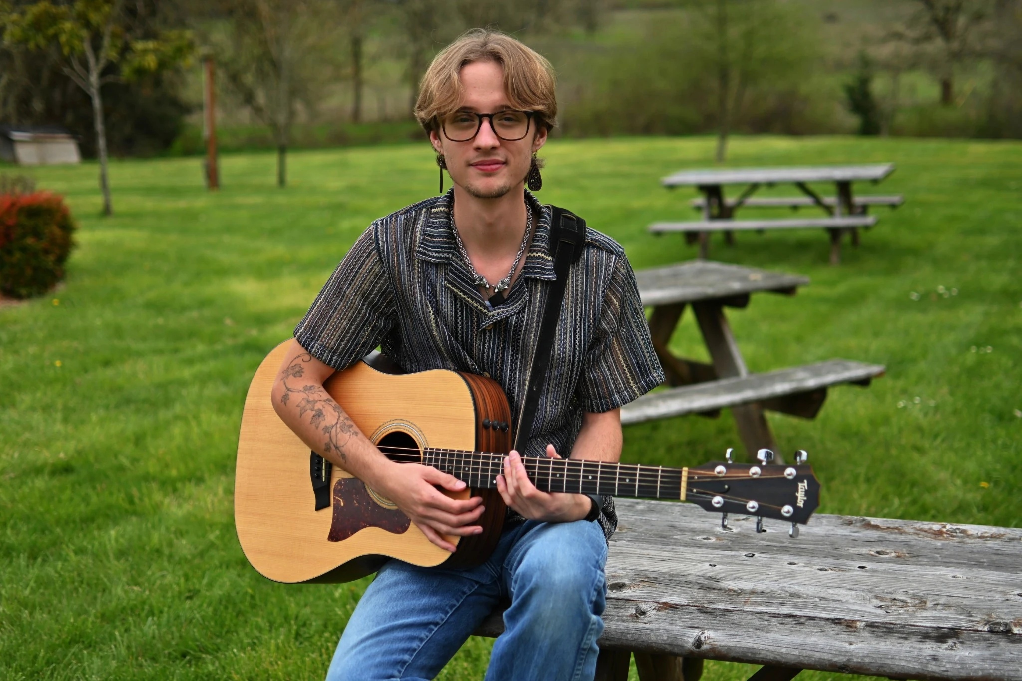 Cooper Morris seated outdoors with an acoustic guitar