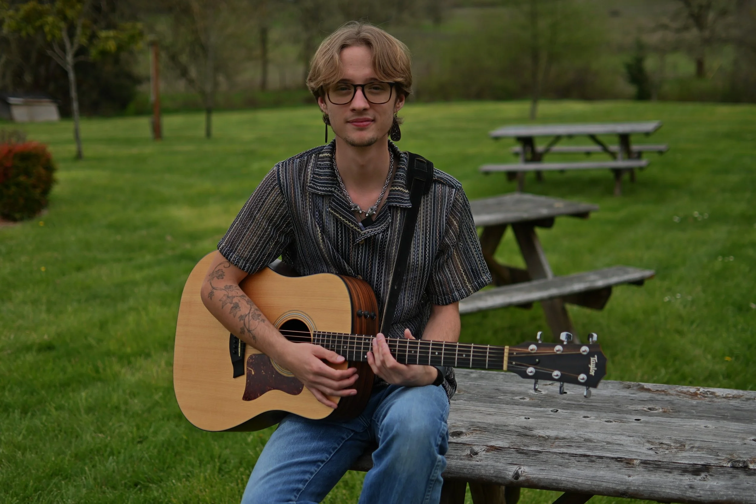 Cooper Morris seated outdoors with an acoustic guitar